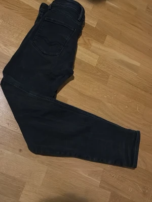 Svarta Replay jeans slim fit - Säljer ett par svarta Replay jeans med slim passform. Klassisk femficksmodell med snygga detaljer på bakfickorna och knappgylf. Jeansen är tillverkade i stretchig bomullsdenim för extra komfort och sitter riktigt snyggt.