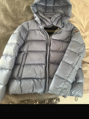 Blå dunjacka med huva från Colmar - Snygg blå dunjacka från Colmar med huva och dragkedja framtill. Jackan har ett quiltat mönster och en rund Colmar-logga på ärmen. Perfekt för kalla dagar och riktigt skön att bära. Klassisk pufferstil som funkar till det mesta.