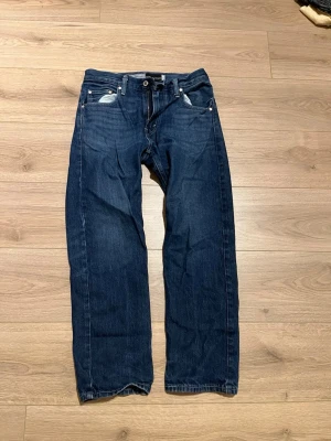 Mörkblå raka Levis jeans - Säljer ett par mörkblå Levis jeans med rak passform och klassiska fem fickor. Jeansen har silverfärgade nitar och knapp, samt kontrastsömmar. Perfekta till en avslappnad stil och tillverkade i mjuk bomull.