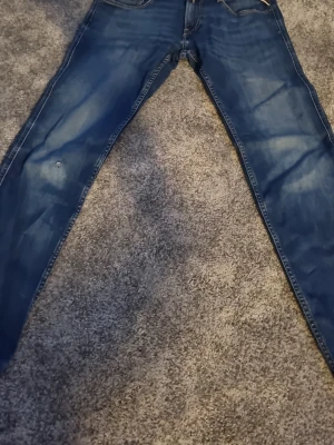 Blå Replay Anbass jeans herr - Säljer ett par blå Replay Anbass jeans med klassisk femficksdesign och snygg tvätt. Jeansen har normal passform och är tillverkade i mjukt bomullsmaterial med lite stretch för extra komfort. Perfekta till vardagslooken!Har ett litet hål på vänster ben men inget man tänker på storlek 30 32