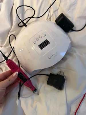 Nagelkit med UV-lampa och elfil - Nagelkit med vit UV-lampa från SUN X och en rosa elektrisk nagelfil. UV-lampan har digital display och tre knappar för timerinställning. Båda verktygen är elektriska och kommer med tillhörande sladdar och adaptrar. Perfekt för hemmabruk när du vill fixa naglarna.