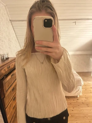 Beige ribbad långärmad tröja - Säljer en beige långärmad tröja med ribbat, vågigt mönster. Tröjan har en rund halsringning och sitter figurnära. Perfekt för en stilren och trendig look.