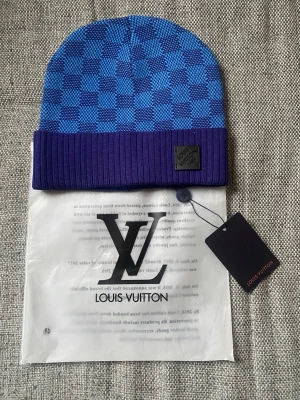 Blå-rutig mössa  -  klassiskt rutmönster i två nyanser av blått och en ribbad kant. Perfekt accessoar för dig som vill sticka ut med stil.