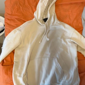 Vit hoodie med huva och magficka - Säljer en enkel vit hoodie med huva och dragsko samt en stor magficka framtill. Hoodien har ribbade muddar vid ärmslut och nederkant. Perfekt för en avslappnad och chill stil.