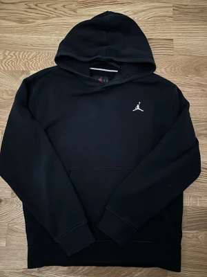 Svart Jordan hoodie med logga - Snygg svart hoodie från Jordan med klassisk Jumpman-logga broderad på bröstet. Hoodien har en stor huva och känguruficka framtill. Perfekt för dig som gillar sportig och avslappnad stil.