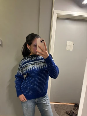 Blå stickad tröja med vitt mönster - Snygg blå stickad tröja med vitt nordiskt mönster över bröstet och axlarna. Tröjan har rund halsringning, långa ärmar och ribbade muddar. Perfekt för kalla dagar och ger en klassisk vinterlook. Tröjan har ingen lapp och ingen storlek men skulle tro att den är S/m, skulle även tro att den är handgjord då den är köpt på second hand