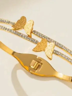 Guldarmband med fjärilar och stenar - Snyggt guld pläterad med två rader, dekorerat med glittrande stenar och tre detaljerade fjärilar i matt guld. Armbandet har en elegant och modern design som passar perfekt till din stil. Metallisk finish och smidig låsning.