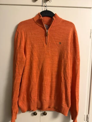 Orange stickad tröja från Morris - Säljer en orange stickad tröja från Morris med ribbad krage och half zip-dragkedja. Tröjan har lång ärm och en liten broderad logga på bröstet. Perfekt för dig som vill ha en färgklick i garderoben.