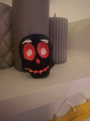 Svart dödskallemaskeradaccessoar - En svart dödskalleaccessoar med stora röda och vita ögon samt röda detaljer vid munnen. Perfekt som dekoration.