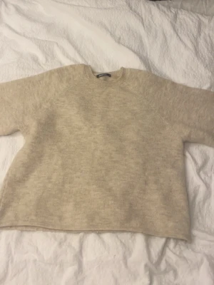 Beige stickad tröja - Mysig beige stickad tröja i oversized modell med rund halsringning och långa ärmar. Tröjan har en enkel och stilren design, perfekt för lager på lager och chill vardagsstil. Materialet ser ut att vara mjukt och lite luddigt, troligen ullblandning.