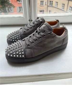 Grå Christian Louboutin sneakers med nitar - Säljer ett par grå sneakers från Christian Louboutin i mocka med silverfärgade nitar över tån. Skorna har snörning och svart sula. Riktigt edgy vibe och perfekta för dig som vill sticka ut med din stil.