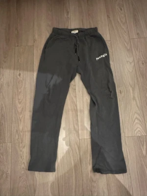 Gråa mjukisbyxor från YoungLA  - Säljer ett par gråa mjukisbyxor från YoungLA med snörning i midjan och tryckt logga på ena benet. Byxorna har en relaxed passform och är perfekta för chill dagar. Tillverkade i mjukt bomullsmaterial för maximal komfort.