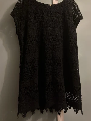 Svart spetsblus med dragkedja - Svart blus i spets med korta ärmar och rund halsringning. Blusen har ett vackert spetsmönster över hela plagget och en dekorativ dragkedja i ryggen. Perfekt för dig som gillar detaljer och en lite dressad look. Köpte den från sellpy, aldrig andvänd.