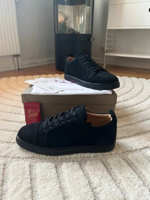 Svarta sneakers från Christian Louboutin - Stilrena svarta sneakers från Christian Louboutin i mocka med klassisk rund tå och svarta snören. Skorna har en låg profil och diskret design med beige innerfoder. Perfekta för dig som gillar lyxiga och minimalistiska sneakers. Box, dustbag och kort medföljer😊 Skickar samma dag.