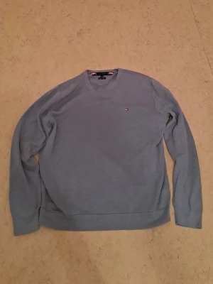 Blå tröja från Tommy Hilfiger - Snygg blå långärmad tröja från Tommy Hilfiger med liten broderad logga på bröstet. Tröjan är i mjuk bomull. Perfekt för dig som gillar stilrena och enkla plagg. I helt nytt skick. Säljs för 300 kr. Först till kvarn som gäller. Tveka inte att kontakta om du är intresserad eller har några frågor!