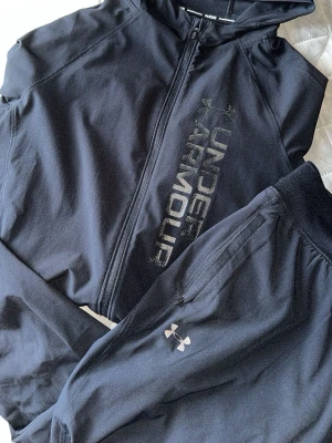 Svart träningsset från Under Armour - Under armour tracksuit. Inga skador, nytt skick. Använt ett par gånger. Storlek S både byxor och koftan