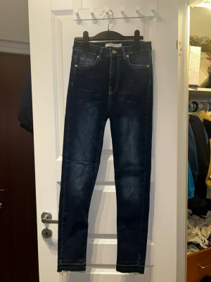 2 par mörkblåa skinny jeans från NA-KD - Säljer två par mörkblå skinny jeans från NA-KD i storlek 34. Jeansen har hög midja, klassiska fem fickor och råa, fransiga benslut för en trendig look. Tillverkade i stretchig denim för skön passform och markerade sömmar. (Båda paren är likadana)