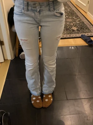 Bootcut low waist ljusa jeans  - Bootcut jeans i ljusblå denim från H&M med låg midja och justerbar midja. Jag har sprättat upp de där nere som på bilden. Du funkar som en storlek 32 skulle jag säga men annars som de står är de barnstorlek 💙
