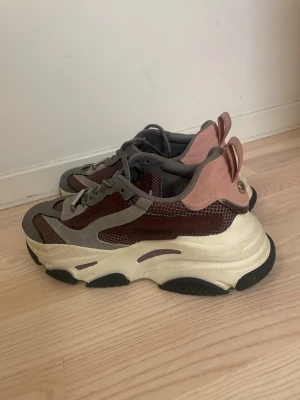 Chunky sneakers från Steve Madden - Chunky sneakers från Steve Madden i en mix av rosa, vinrött och grått. Skorna har meshdetaljer, mockaliknande partier och en rejäl vit plattformssula med svarta detaljer undertill. Klassisk snörning och cool retrostil som sticker ut. 