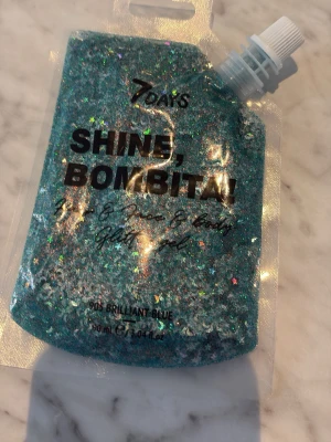7 Days Shine Bombita Glitter Gel - Glittrig gel i färgen Brilliant Blue från 7 Days. Kommer i en smidig plastpåse med skruvkork och innehåller 90 ml. Gelen har stora och små glitterpartiklar i blått och holografiska nyanser, perfekt för hår, ansikte och kropp. Superenkel att applicera för en maxad gloweffect.