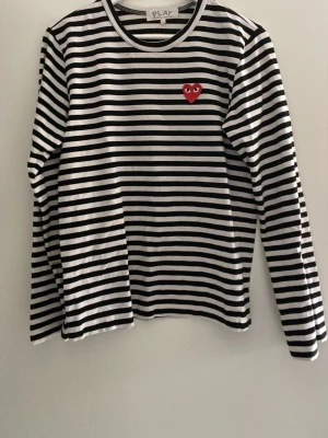 Comme des Garçons longsleeve - Säljer en svartvit randig långärmad t-shirt från Comme des Garçons PLAY med det ikoniska röda hjärtat med ögon broderat på bröstet. Klassisk rund halsringning och mjukt bomullsmaterial. Storlek L men sitter som M
