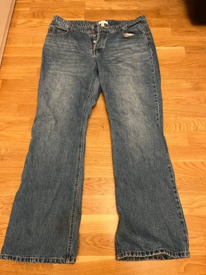 Blå raka jeans från H&M, strl 48 - Klassiska blå jeans från H&M i rak modell med normal passform. Jeansen har knappgylf, fem fickor och är tillverkade i slitstarkt bomullsmaterial. Perfekta för en avslappnad och tidlös look.