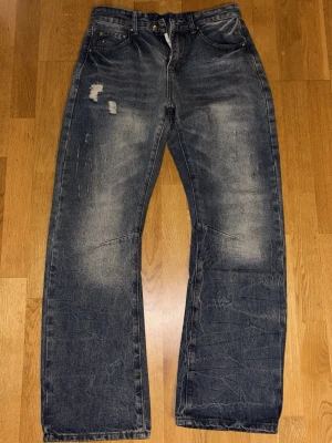  blå jeans bootcut - Säljer ett par jeans i blå tvätt med slitningar och bootcut passform. Jeansen har fem fickor, normal midja och är tillverkade i  denim. Snyggt slitna detaljer framtill för en avslappnad look. Perfekta till sneakers eller boots. Storlek 31 midja 32 längd.