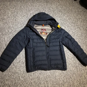 Mörkblå dunjacka från Parajumpers - Säljer en mörkblå Parajumpers dunjacka med huva och dragkedja. Jackan är superlätt och har quiltad design samt en snygg gul detalj vid axeln. Insidan är ljusgrå och materialet är syntet med dunfyllning. Perfekt för kalla dagar och riktigt skön att bära. Extra bra nu inför sen vinter och vår.  Pris kan diskuteras. 😊