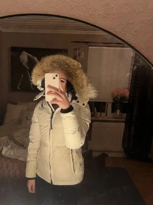 Äkta Vit Canada Goose jacka - Säljer en snygg vit jacka från Canada Goose med stor fluffig päls runt huvan. Jackan har dragkedja framtill, två fickor med dragkedja och klassisk patch på ärmen. Perfekt för kalla dagar och riktigt varm. Använt många vintrar men forfarande jätte bra skick på jackan. 