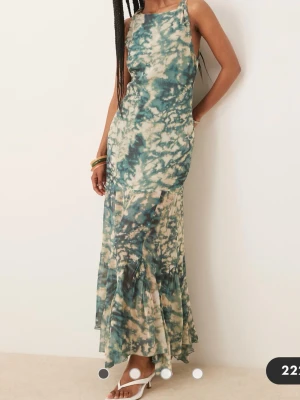 Långklänning med batikmönster - Supersnygg långklänning med batikmönster i grönt och beige. Klänningen har ärmlös design och rund halsringning. Nertill är den transparent och har volangdetaljer. Luftigt material som passar perfekt för varma dagar och ger en avslappnad men trendig look.