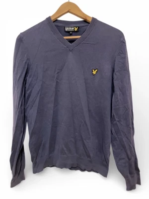 Mörkblå tröja från Lyle & Scott - Snygg mörkblå tröja från Lyle & Scott med klassisk v-ringning och gul logga på bröstet. Tillverkad i 100% bomull för en skön känsla. Perfekt till jeans eller chinos för en clean look.