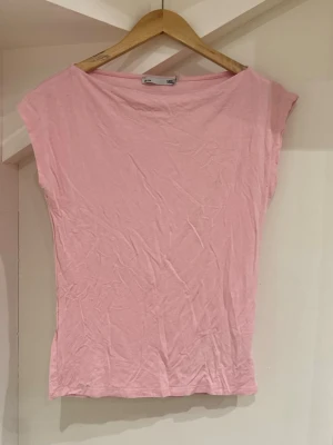 Ljusrosa topp från 157, storlek M - Enkel och stilren ljusrosa topp från 157 i mjuk bomull. Modellen är ärmlös med rund halsringning och har en rak, något loose passform. Perfekt att matcha med jeans eller kjol för en avslappnad look.