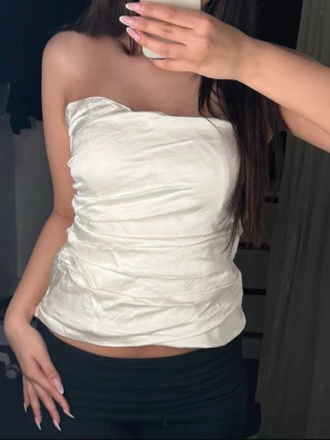 Vit bandeau topp - Säljer en snygg vit bandeau tubtopp från Zara i glansigt satinliknande material. Toppen är axelbandslös och har en lätt rynkad effekt på sidorna som ger en super fin look. Storlek S köp direkt för 219kr via köp nu💞😍😍
