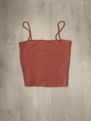 Rostfärgad linnetopp från H&M Divided - Säljer en enkel och snygg rostfärgad linnetopp från H&M Divided. Toppen har tunna axelband och rak skärning, perfekt till sommaren. Tillverkad i mjuk bomull som känns skön mot huden.