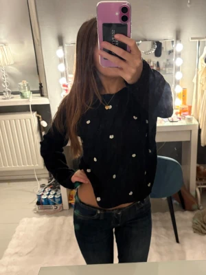 Svart stickad tröja med blommor Mademoiselle R - Svart stickad tröja från Mademoiselle R med vita broderade blommor över hela tröjan. Modellen är lite croppad och har långa ärmar. Perfekt för dig som vill ha en söt och mysig look med en twist, lite stickig så man får ha ett linne undertill.❣️