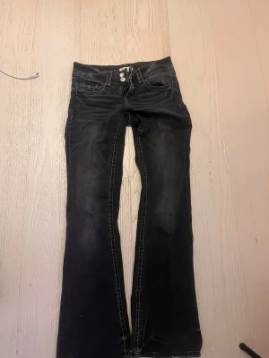 Svarta bootcut jeans Gina Tricot 158 - Säljer ett par svarta bootcut jeans från Gina Tricot i storlek 158. Jeansen har dubbla knappar i midjan, klassiska fem fickor och snygga slitningar. Materialet är jeans med tydliga sömmar och en lite tvättad look.