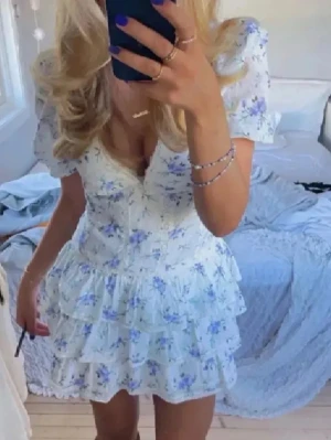 Blommig kortklänning med volanger - Supersöt kortklänning med blommönster. Klänningen har puffiga korta ärmar, djup v-ringning och flera lager volanger i kjolen. Perfekt för sommarens alla tillfällen! Jag köpte den begagnat, men då den inte passar mig säljer jag den vidare. 