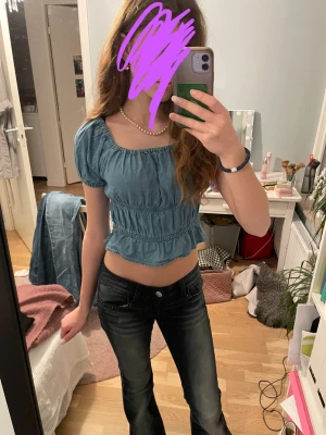 Blå croppad blus med volang - Söt blå croppad blus med puffärmar och volangkant nertill. Toppen har resår i midjan och runt halsen för en bekväm passform. Perfekt till jeans eller kjol för en trendig look. Köpt i amsterdam.
