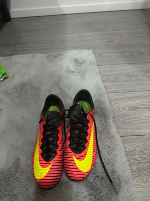 Nike mercurial vapor 11 elite ag - Säljer ett par Nike fotbollsskor med snyggt randigt mönster i rött och svart, samt stora gula swoosh-loggor på sidorna. Skorna har snörning och dobbar för gräsplan. Insidan är grön och materialet är syntet för bästa prestanda på planen. Skorna är sällsynta och är väldigt svåra att få tag på