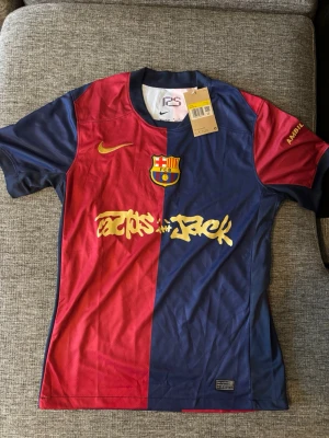 Barça x Nike Travis Scott matchtröja - Säljer en limited edition FC Barcelona x Travis Scott matchtröja från Nike. Tröjan är röd och marinblå med gul logga och tryck, tillverkad i 100% polyester med Dri-Fit-teknologi. Halva tröjan är röd, andra halvan blå, och har klubbmärke samt Travis Scott-grafik framtill.