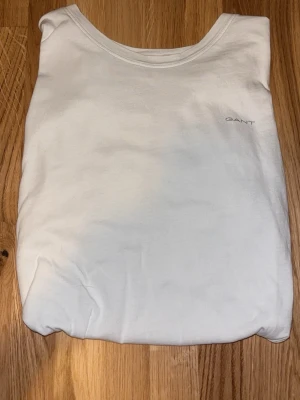 Vit t-shirt från GANT i bomull - Klassisk vit t-shirt från GANT med diskret logga på bröstet. Tillverkad i mjuk bomull och har en enkel, rund halsringning. Perfekt basplagg för alla tillfällen och enkel att matcha med andra plagg.