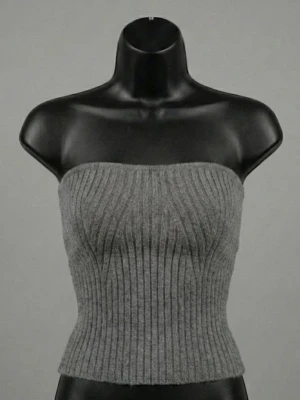 Grå ribbad stickad tubtopp - Säljer en grå ribbad tubtopp i stickat material. Toppen är axelbandslös och har en bandeauformad passning som sitter snyggt och tight mot kroppen. Perfekt att styla med höga jeans eller kjol för en trendig look.