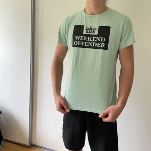 Weekend Offender mintgrön t-shirt - Snygg mintgrön t-shirt från Weekend Offender med svart och vit logga på bröstet. Klassisk rund hals och korta ärmar. Perfekt för dig som gillar streetwear och vill sticka ut med en fräsch färg. Skön passform och mjukt material.