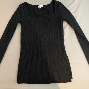 Svart ribbad långärmad topp Bik Bok - Svart långärmad topp från Bik Bok med ribbad struktur och fyrkantig ringning med slits vid sidorna. Toppen är figurnära och har en mjuk, stretchig känsla.