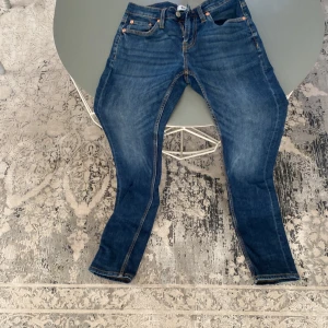 Blå jeans i storlek S - Snygga blå jeans med stiliga detaljer i storlek S. Klassisk femficksmodell med dragkedja och knapp framtill. Jeansen har en rak passform och är tillverkade i slitstarkt denimtyg med orangea sömmar. Perfekta för en avslappnad och trendig look.