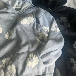 Denim Tears hoodie  - Säljer en hoodie från Denim Tears med unikt blommönster. Finns i både ljusgrått med vita blommor och svart med grå blommor. Hoodien har huva och är tillverkad i mjuk bomullsblandning, perfekt för en chill och trendig look.