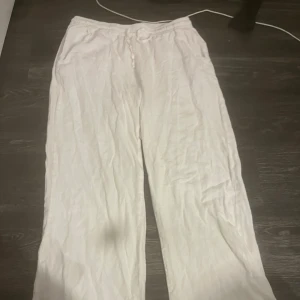 Vita linnebyxor med snörning - Säljer ett par vita linnebyxor med avslappnad passform och dragsko i midjan. Byxorna har raka ben, resår i midjan och en bakficka. Perfekta för varma dagar och chill vibes.