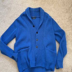 Blå stickad kofta från Filippa K - Säljer en blå stickad kofta från Filippa K med sjalkrage och svarta knappar framtill. Koftan har två stora fickor och är ribbstickad. Storlek small men passar lite större.