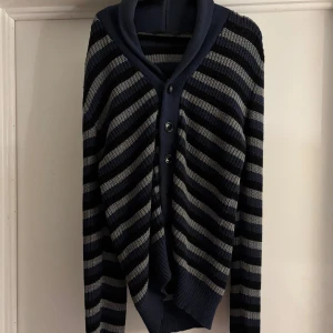 Randig cardigan från Filippa K  - Snygg randig kofta från Filippa K i marinblått och grått. Koftan är stickad med bred krage och knäpps med knappar framtill. Perfekt för lager-på-lager och chill höststil.