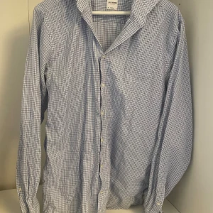 Rutig skjorta från John Henric - Knappt använd och nypris 1099kr.                  Snygg blå- och vitrutig skjorta från John Henric med klassisk krage och knäppning framtill. Tillverkad i mjuk bomull med italienskt tyg, perfekt för en clean och stilren look. Långärmad modell med diskreta knappar.